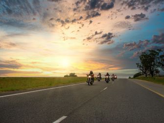 A group of motorcyclists riding on a highway during sunset with a cloudy sky.