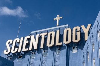 Sign of the Church of Scientology with a cross on top, against a blue sky.