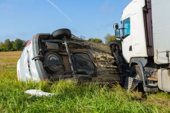 A truck and a flipped vehicle in a field, illustrating the aftermath of a trucking accident.