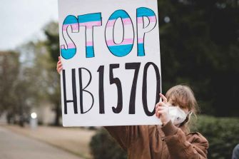 Person holding a sign that says "STOP HB1570," protesting against the law banning youth gender-affirming treatment in Arkansas.