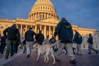A group of law enforcement officers with a dog approach the Capitol building during heightened security measures leading up to the inauguration.