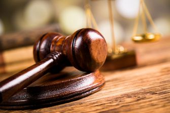 A wooden gavel resting on a circular base, with a background of blurred scales of justice, symbolizing legal proceedings and court rulings.