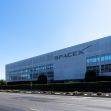 Exterior view of the SpaceX building with a rocket launch pad in the background. Exterior view of the SpaceX building with a rocket launch pad in the background.