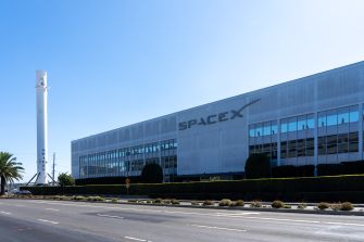 Exterior view of the SpaceX building with a rocket launch pad in the background.