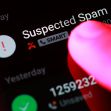 A finger pressing a smartphone screen displaying a "Suspected Spam" notification on an incoming call. A finger pressing a smartphone screen displaying a "Suspected Spam" notification on an incoming call.