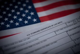 A close-up of a U.S. birth certificate displayed alongside the American flag.