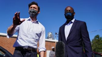Two candidates for the Georgia runoff elections, Jon Ossoff and Raphael Warnock, speaking together outdoors while wearing masks.