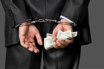 A businessman in a suit is handcuffed while holding cash, symbolizing fraud and legal consequences.