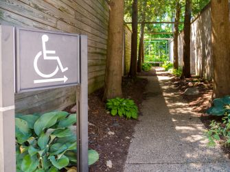 A path marked with a disability access sign, surrounded by greenery and wooden fencing.