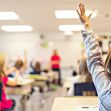 A classroom setting with students raising their hands, focusing on a teacher in the background. A classroom setting with students raising their hands, focusing on a teacher in the background.