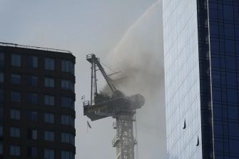 Crane on fire during collapse in Manhattan, surrounded by buildings.