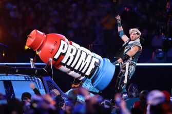 Logan Paul performing with a large promotional display of Prime Hydration drink at a wrestling event.