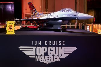 A model F-16 fighter jet displayed with promotional signage for 'Top Gun: Maverick,' featuring the names Tom Cruise and the film's title.