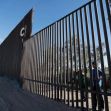 Children looking through gaps in a section of the border wall. Children looking through gaps in a section of the border wall.