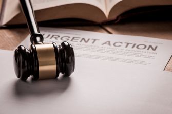 Image of a gavel resting on a sheet of paper labeled "URGENT ACTION," with a law book in the background.