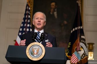 President Biden delivering a speech on the "Buy American" Executive Order, with the Presidential Seal and American flags in the background.