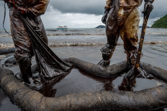 Workers in protective gear cleaning up an oil spill on a polluted shoreline.