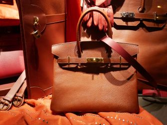 A brown Hermès Birkin handbag displayed with other luxury items.