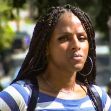 A Black transgender woman looking directly at the camera, outdoors, wearing a striped shirt and hoop earrings. A Black transgender woman looking directly at the camera, outdoors, wearing a striped shirt and hoop earrings.