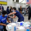A healthcare worker administering a COVID-19 vaccine to an individual in a vaccination center, with officials observing in the background. A healthcare worker administering a COVID-19 vaccine to an individual in a vaccination center, with officials observing in the background.