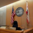 Image of a courtroom with flags and a seal of California, featuring a judge's bench and signage that reads "Patience - Courtesy." Image of a courtroom with flags and a seal of California, featuring a judge's bench and signage that reads "Patience - Courtesy."