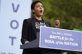 A woman speaking at a podium during a voting event, advocating for civic engagement and addressing community issues.
