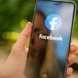 A hand holding a smartphone displaying the Facebook logo on the screen. A hand holding a smartphone displaying the Facebook logo on the screen.