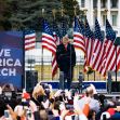A crowd with smartphones gathers as a speaker addresses the audience at the "Save America March" event, with American flags in the background. A crowd with smartphones gathers as a speaker addresses the audience at the "Save America March" event, with American flags in the background.