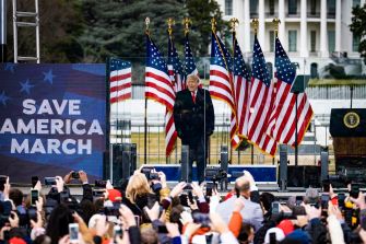 A crowd with smartphones gathers as a speaker addresses the audience at the "Save America March" event, with American flags in the background.