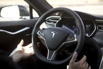 Image of a Tesla steering wheel and dashboard, illustrating the vehicle's interior with driver hands potentially engaged in controlling the car.