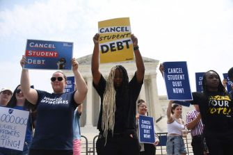 Protesters hold signs advocating for student debt cancellation outside the Supreme Court building.