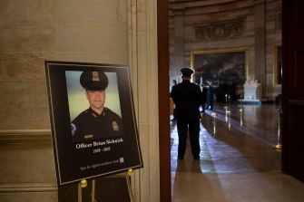 A memorial portrait of Officer Brian Sicknick displayed in the Capitol building, with a Capitol Police officer standing in the background.