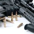 A close-up of a firearm setup featuring an assault rifle, a magazine, and ammunition rounds on a surface. A close-up of a firearm setup featuring an assault rifle, a magazine, and ammunition rounds on a surface.
