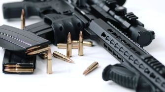 A close-up of a firearm setup featuring an assault rifle, a magazine, and ammunition rounds on a surface.
