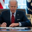 President Biden signing documents at a desk in the Oval Office, with American flags and family photos in the background. President Biden signing documents at a desk in the Oval Office, with American flags and family photos in the background.