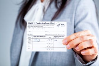 A person holding a COVID-19 vaccination record card, displaying vaccination details.