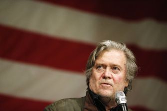 Steve Bannon speaking at an event with an American flag backdrop.