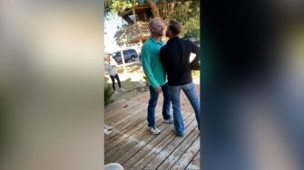 Confrontation between two men outside a home, with a third person in the background.
