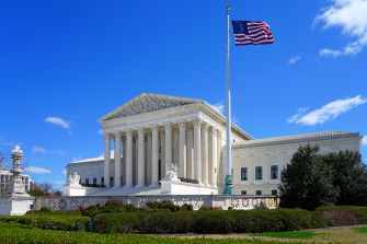 Image of the U.S. Supreme Court building with an American flag flying in front against a clear blue sky.
