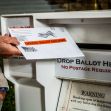 Person placing an official ballot envelope into a drop box labeled "Drop Ballot Here" with a warning sign about tampering. Person placing an official ballot envelope into a drop box labeled "Drop Ballot Here" with a warning sign about tampering.