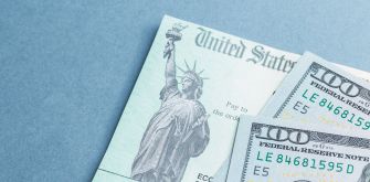 Image of a U.S. stimulus check with the Statue of Liberty and U.S. currency notes.