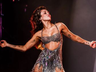 Miley Cyrus performing on stage in a shimmering outfit.