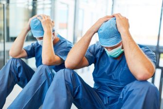 Two hospital staff members in scrubs and masks sitting on the floor with their heads in their hands, appearing distressed.