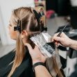A woman getting her hair dyed in a salon, with foils in her hair and a stylist applying color. A woman getting her hair dyed in a salon, with foils in her hair and a stylist applying color.