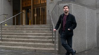 A man standing on the steps outside a courthouse, dressed casually in a dark jacket and sweater.