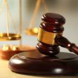 A gavel resting on a wooden block with scales of justice in the background. A gavel resting on a wooden block with scales of justice in the background.