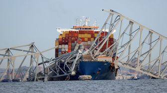 A cargo ship with a toppled section of the Francis Scott Key Bridge in the background, illustrating the aftermath of a maritime accident.