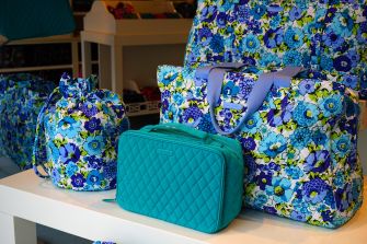 Display of Vera Bradley bags and accessories with a floral pattern and a teal-colored handbag.