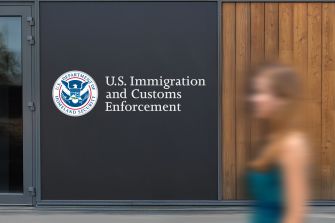 Sign of U.S. Immigration and Customs Enforcement (ICE) with a blurred figure in the foreground.