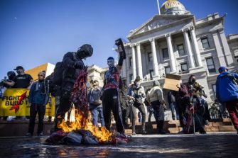 Protesters burning an American flag during a demonstration in front of a governmental building.